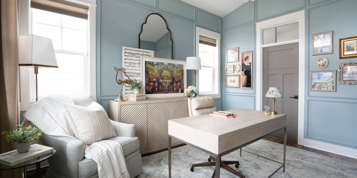 Elegant home office with blue walls, cozy armchair, and modern desk setup.