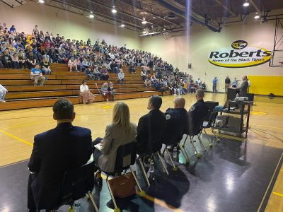 Panelists address a large audience in a school gymnasium.