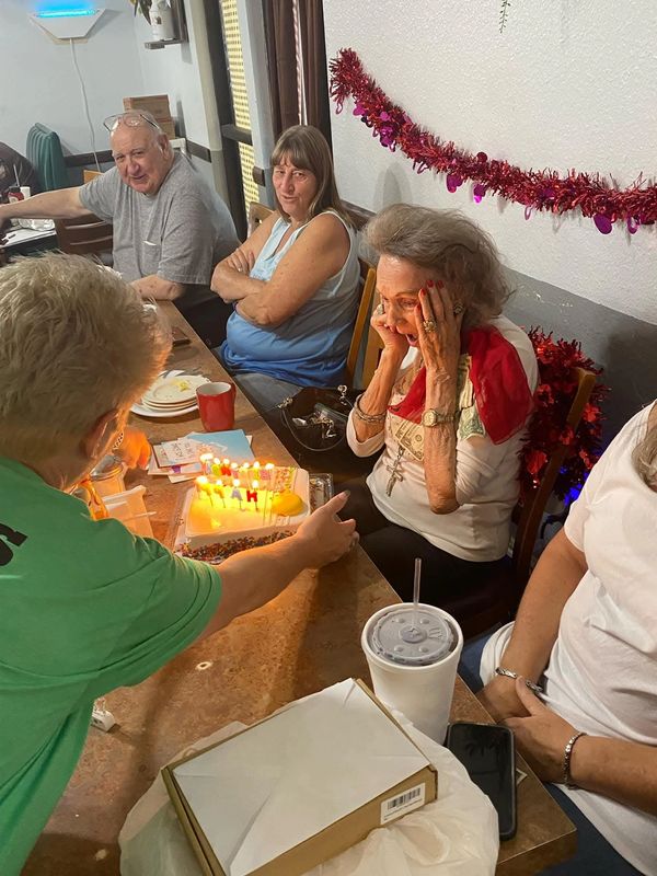 Elderly woman surprised by birthday cake surrounded by family.