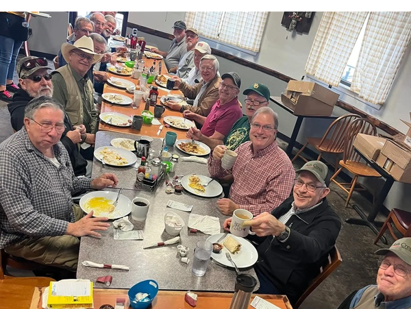 Group of men enjoying breakfast together at a long dining table.