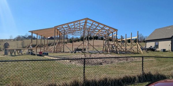 Wooden frame of a large building under construction in a rural area.
