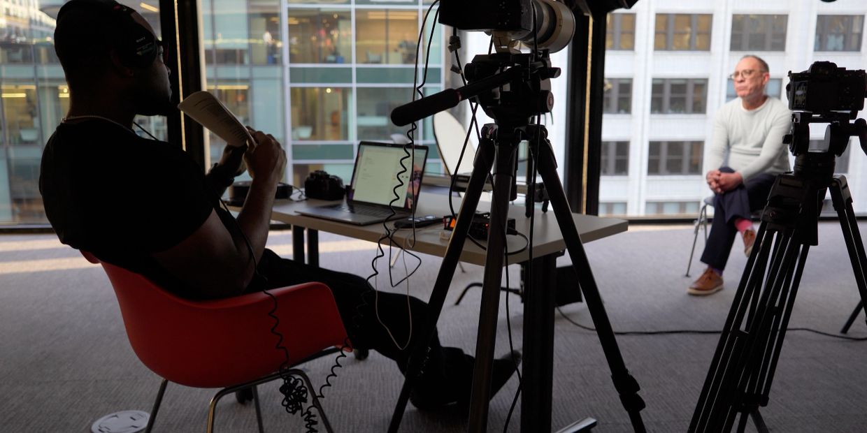 Two men engaged in a video interview setup in an office with cameras and laptops.