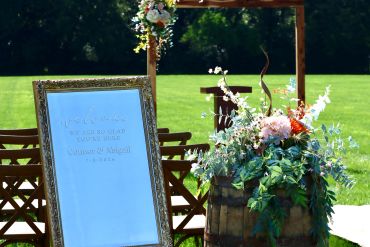 Wedding welcome sign and floral arrangement outdoors.