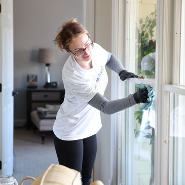 Image of a woman cleaning a window inside with a cloth