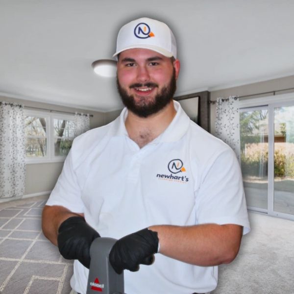 Man in branded uniform cleaning carpet with machine in a bright room.