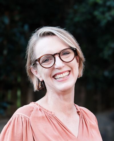 Smiling woman with glasses in a peach blouse outdoors.