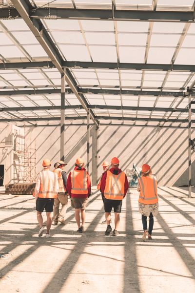 Construction workers wearing safety vests and helmets walking inside a building framework.