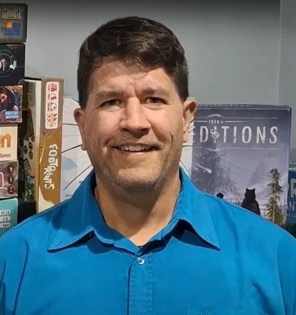 Man in blue shirt smiling with board games behind him.