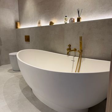 Modern white freestanding bathtub with gold fixtures.