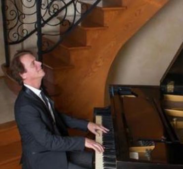 Man playing piano near wooden staircase.