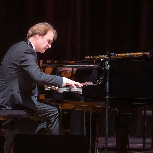 Man playing grand piano on stage.