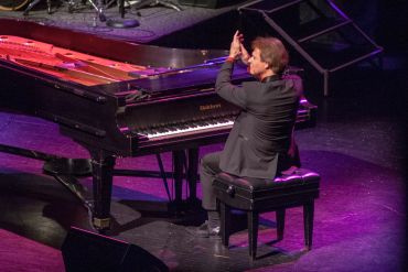Man applauding at a grand piano on stage.