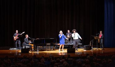 A band performs on stage with a female singer and musicians.