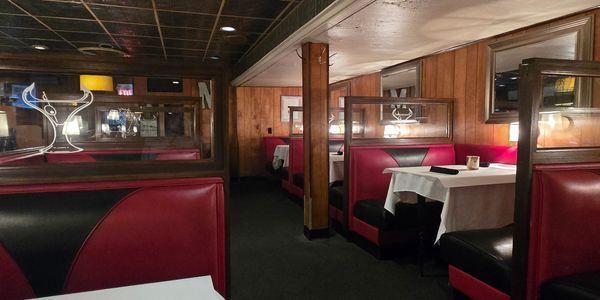 Cozy restaurant booths with red and black seats and white tablecloths.