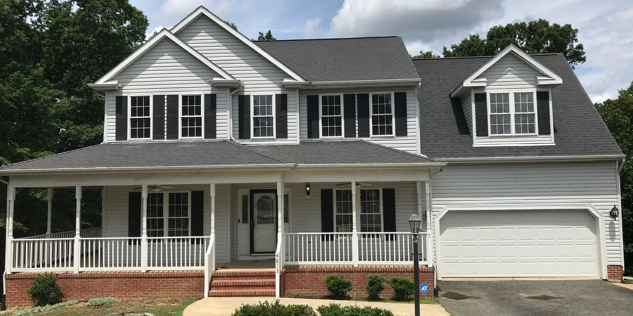 Colonial home with grey siding, a front-loading garage, and a wrap-around porch.
