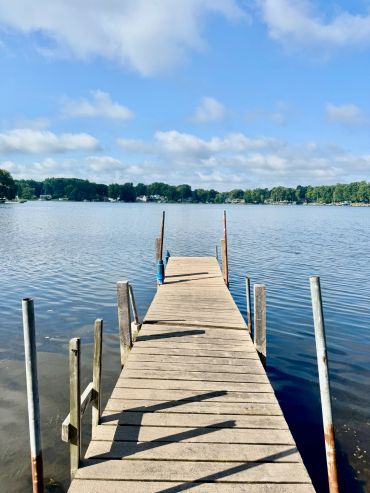 Wooden dock extending into a calm lake under a blue sky.