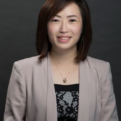 Professional woman in blazer smiles against a dark background.