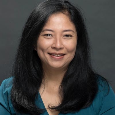 Smiling woman with long black hair against a gray background.