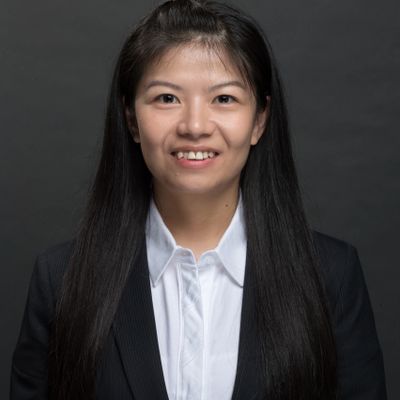 Professional portrait of a smiling young woman with long black hair in a suit.