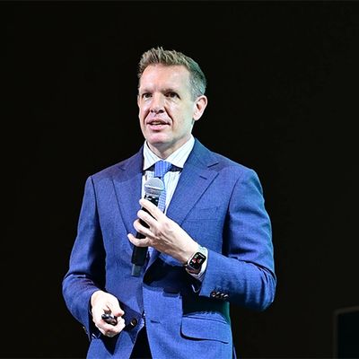 Man in blue suit speaking on stage with a microphone.