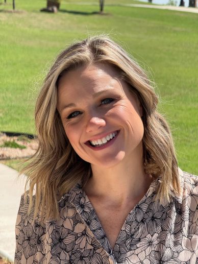 Smiling woman outdoors with flower-patterned blouse.