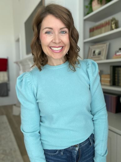 Smiling woman in a blue sweater indoors.