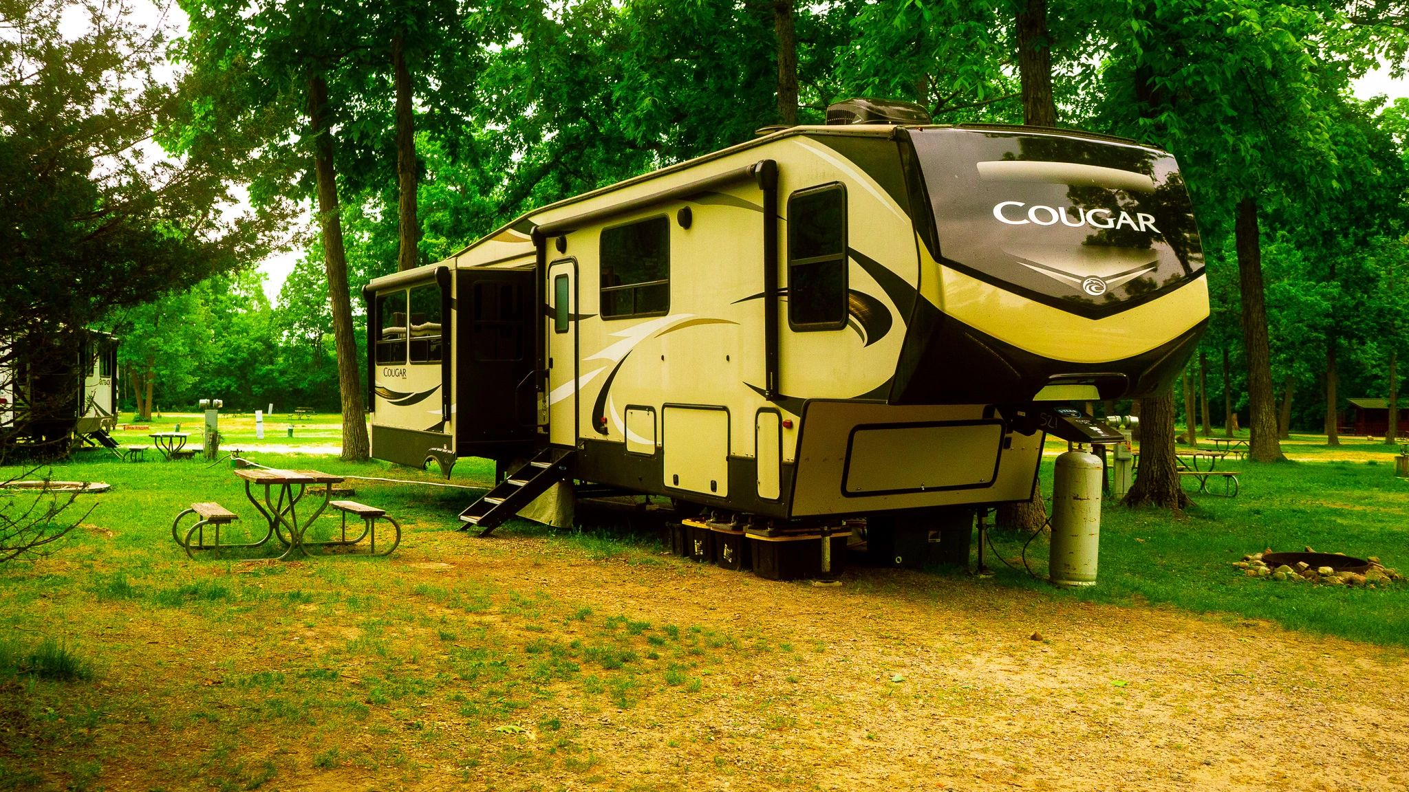 A Cougar RV parked in a green, wooded campground.