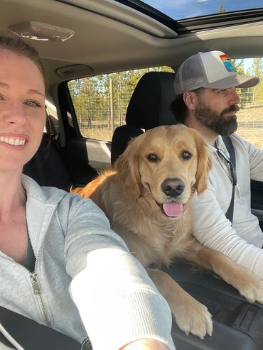 A happy couple with a golden retriever dog in a car.