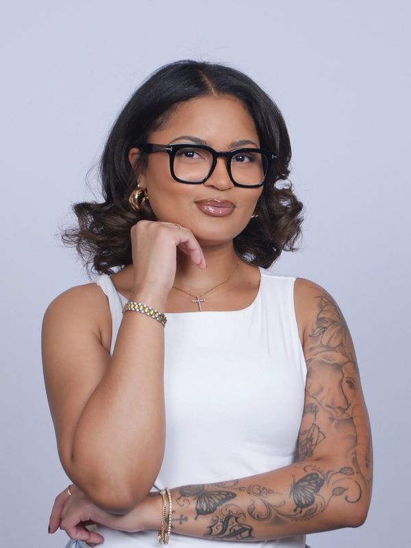 Confident woman with glasses and tattooed arm posing thoughtfully.
