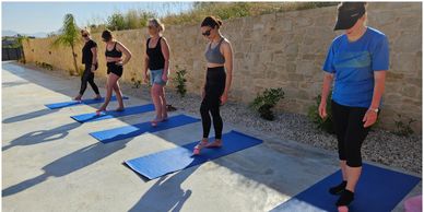 Group practicing yoga or stretching on mats outdoors in sunny weather.