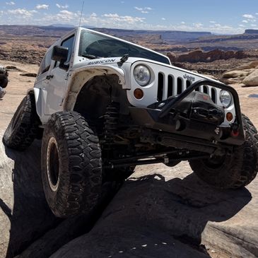 White Jeep navigating deep snow in a forest.