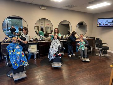 Children getting haircuts in a salon with stylists at work.