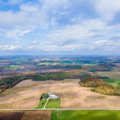 Aerial view of vast farmland with a farmhouse under a partly cloudy sky.