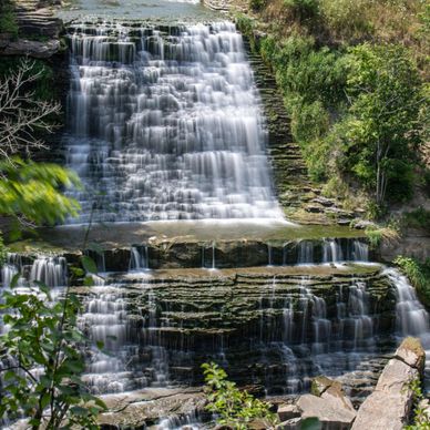 A multi-tiered waterfall cascading over rocky ledges surrounded by greenery.