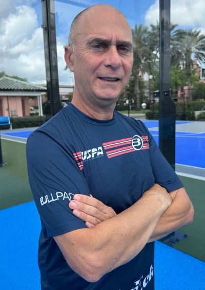 Man in sportswear with arms crossed on a tennis court.