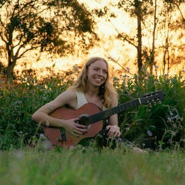 Young woman playing guitar outdoors at sunset with a joyful smile.