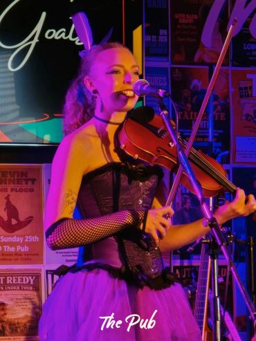 Female violinist singing on stage at The Pub with vibrant lighting.