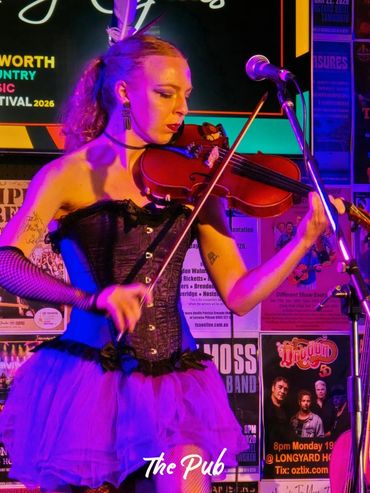 Woman in a purple tutu playing violin on stage at The Pub.