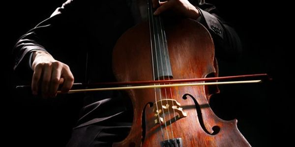 A person playing a cello with a bow in dim lighting.