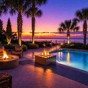 A luxurious poolside patio at sunset with fire pits and palm trees.