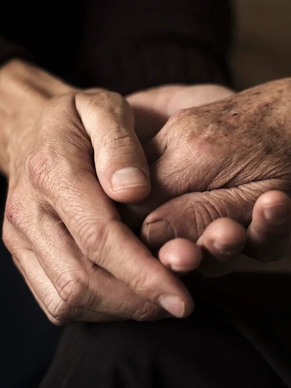 Two aged hands tenderly holding each other, symbolizing care and comfort.