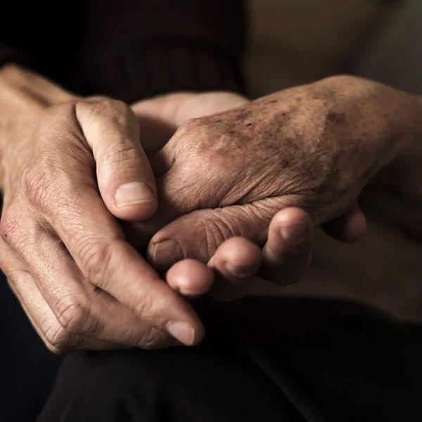 The hands of one person gently cupping the hand of an elderly person. 