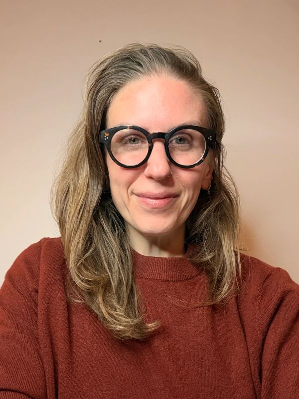 Woman with round black glasses and brown sweater smiling.