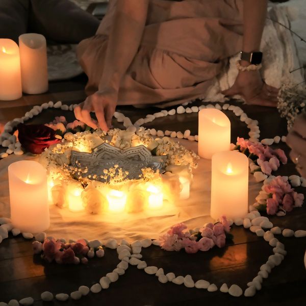 A woman tends to an floor mandala arrangement with candles, small flowers, and little white stones.