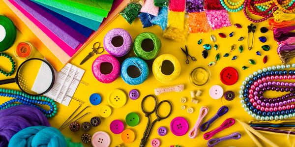 Colorful craft supplies including buttons, threads, beads, and scissors on a yellow background.