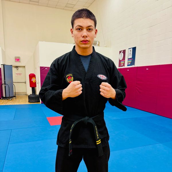 Young martial artist in a black gi with a black belt inside a gym.
