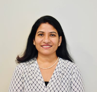 Smiling woman with long black hair wearing a patterned blouse and pearl necklace.
