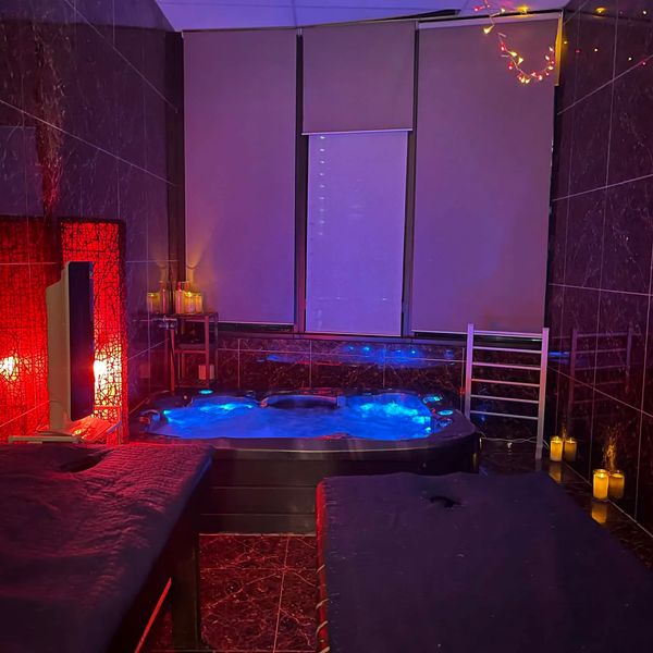 A cozy spa room with a glowing blue hot tub and soft ambient lighting.