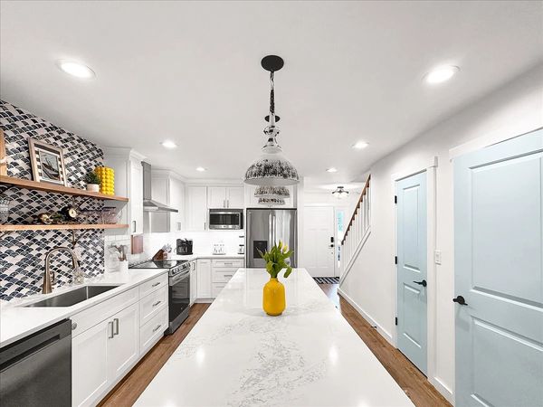 Modern white kitchen with a large marble island and light blue doors.