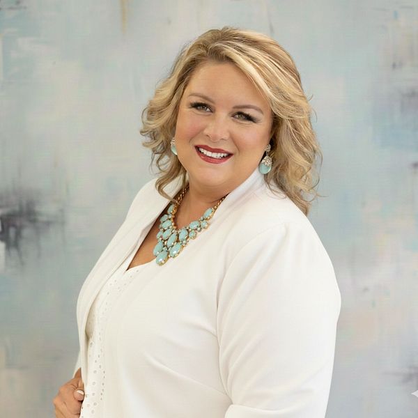Smiling woman in white outfit with turquoise jewelry against a soft background.